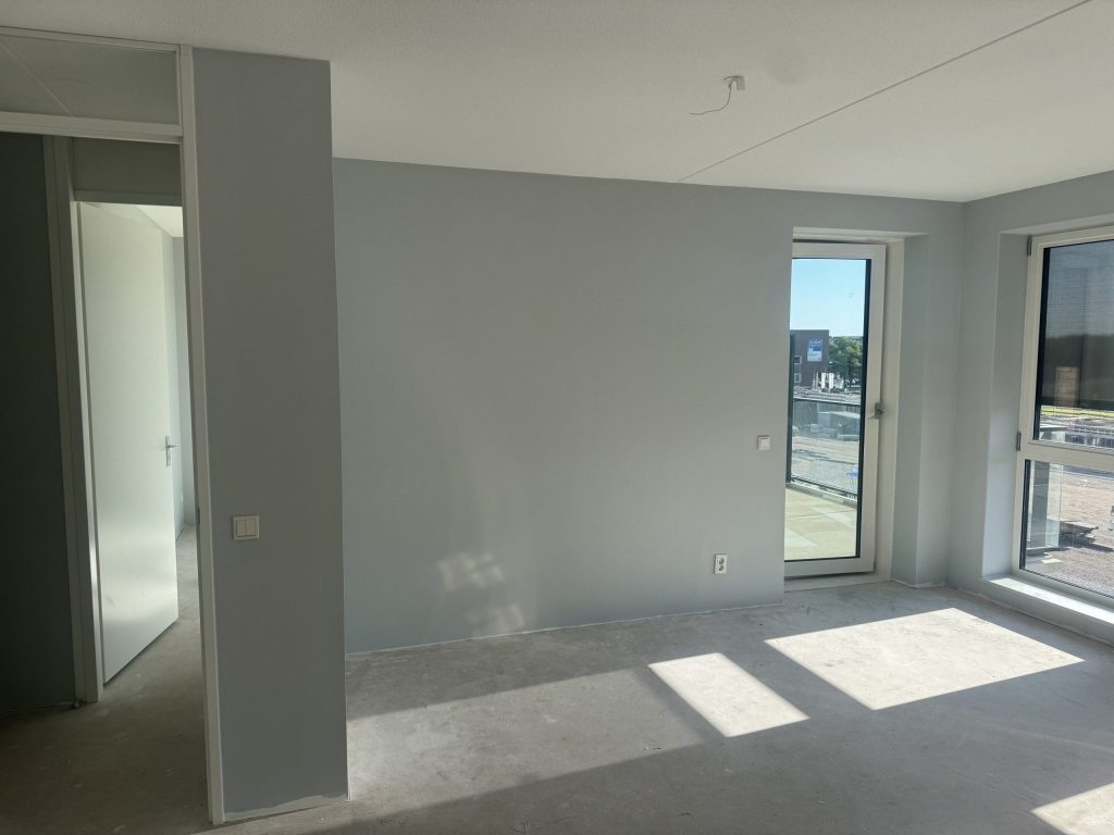 Nieuw appartement met lichtgrijze, egaal afgewerkte wanden en zonlicht door de balkondeur