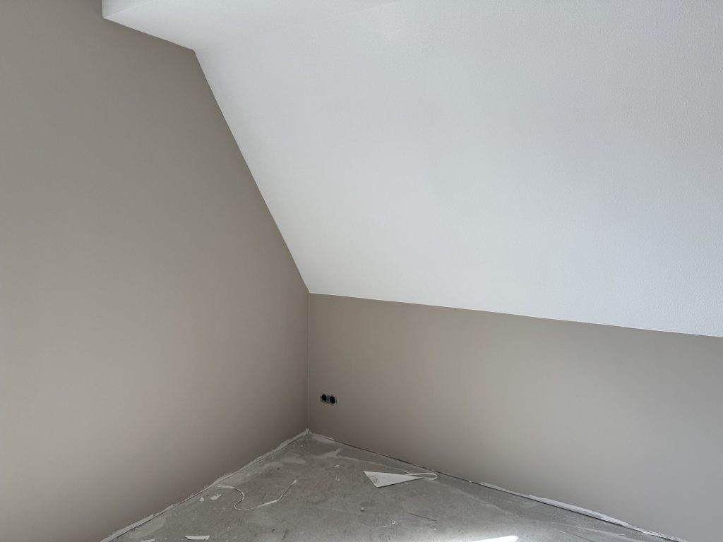Zolderkamer met een schuine wand, afgewerkt in een warme zandkleur onder een wit dakvlak