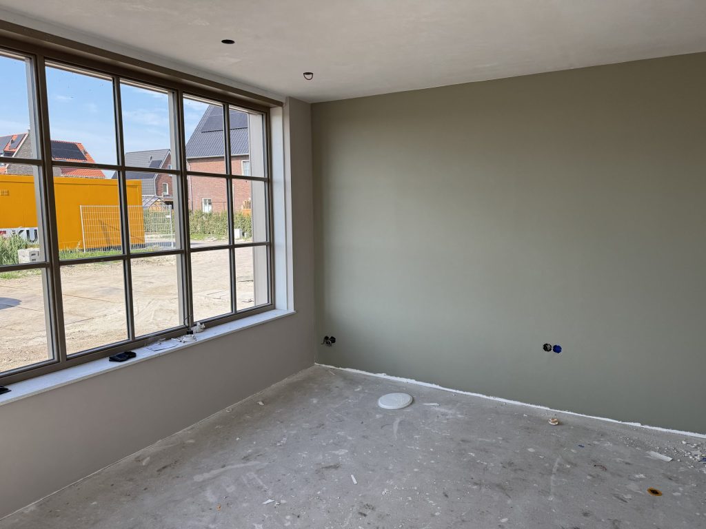 Kamer met een groot roedenraam en een strakke wand in groengrijs, net na het sauzen