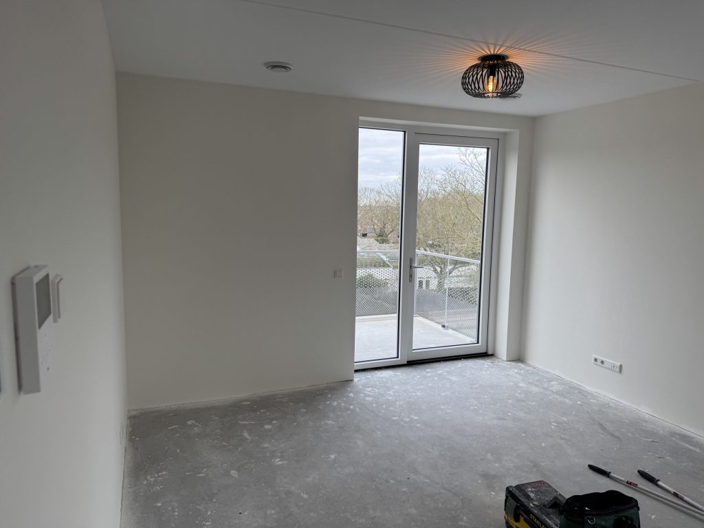 Lichte, lege kamer met gladde witte wanden en openslaande deuren naar het balkon